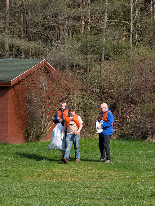 Students walking teacher holding trash bags