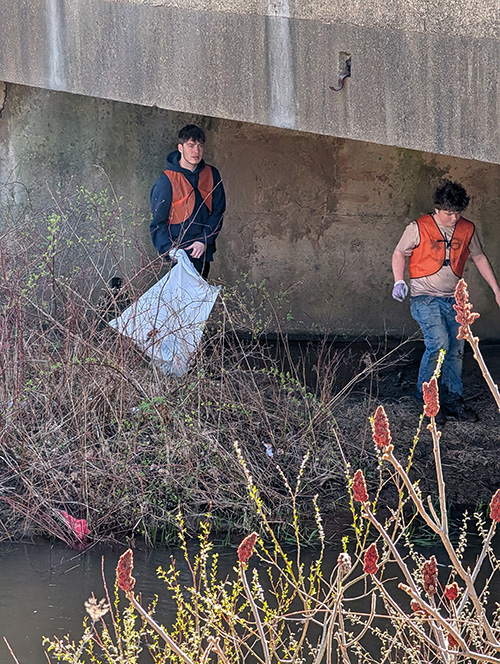 Students cleaning trash under an embankment area
