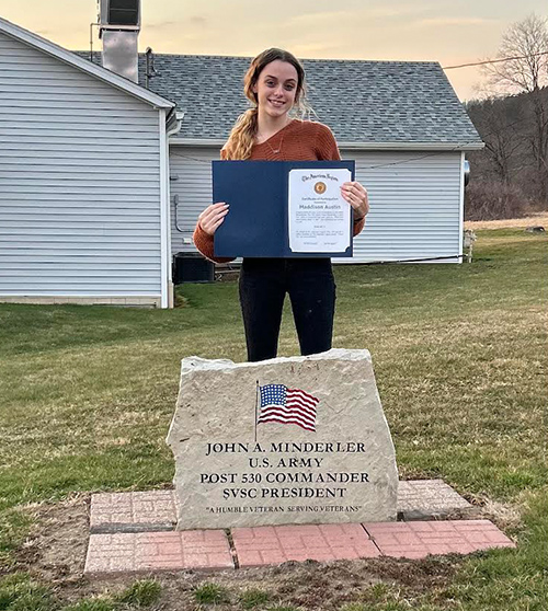 Madison holding award outside next to Shinglehouse American Legion Post 530 sign