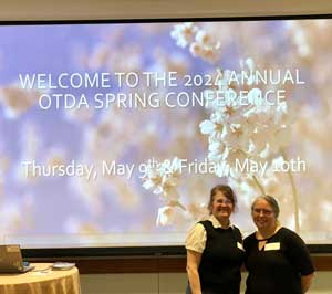 Mrs. Lana Brath and Mrs. Kim Mooney standing in front of conference welcome sign